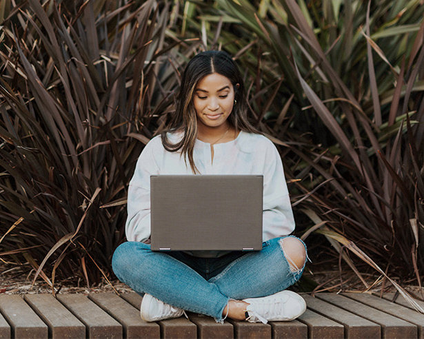 Woman working on laptop sitting on a bench outside